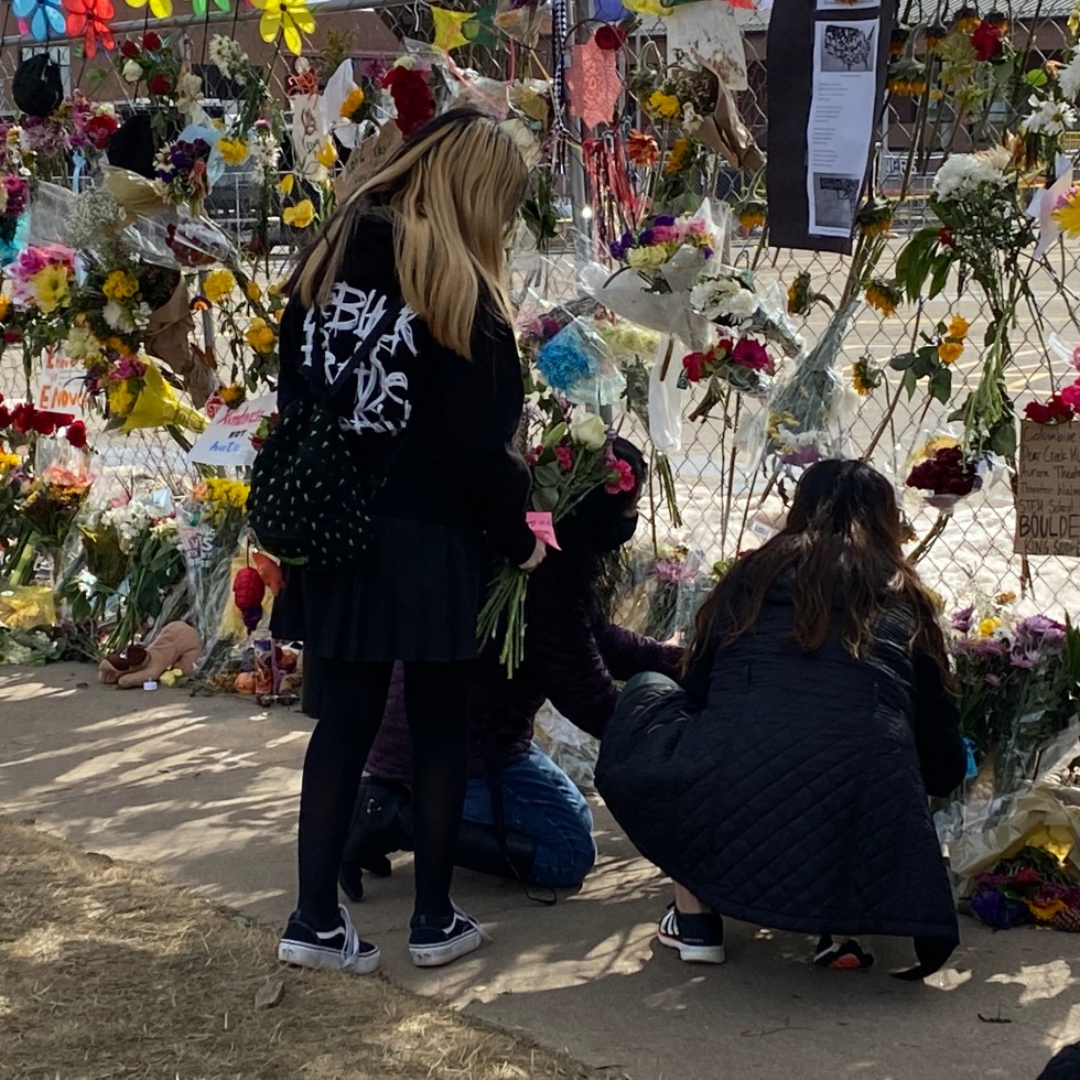 Three young women place flowers at the memorial site set up around the perimeter of the Table Mesa King Soopers parking lot.